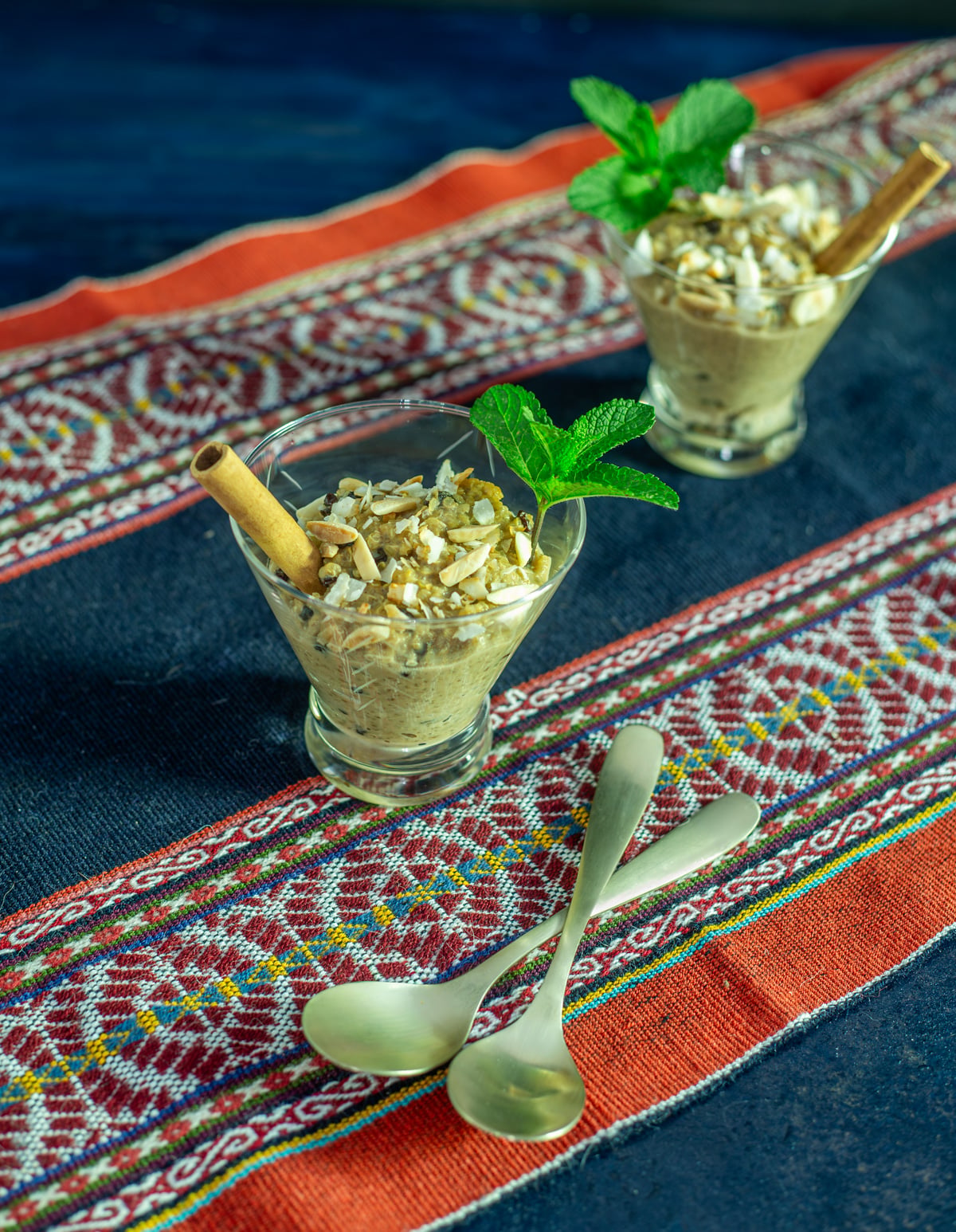 A colorful textile with 2 glass cups with quinoa con leche and 2 spoons.