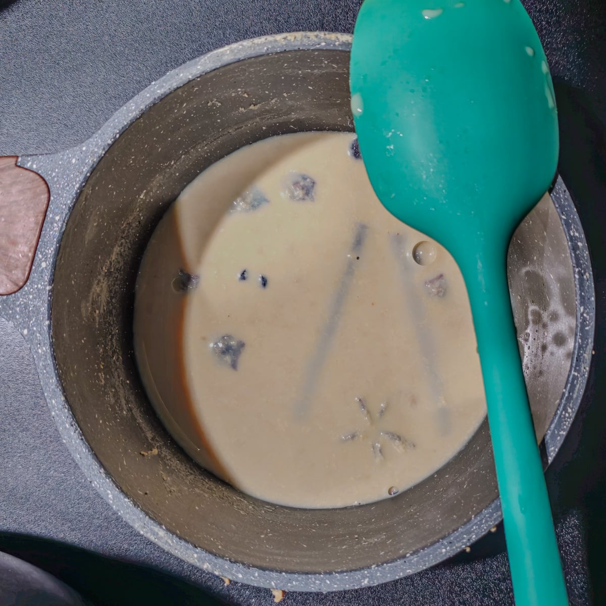 Milk is infused with cinnamon, cloves, and star anise in a small saucepan.