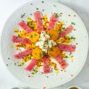 The prepared Tiradito de At&uacute;n on an embossed white ceramic plate with sweet potatoes, maiz mote, and garnishes.