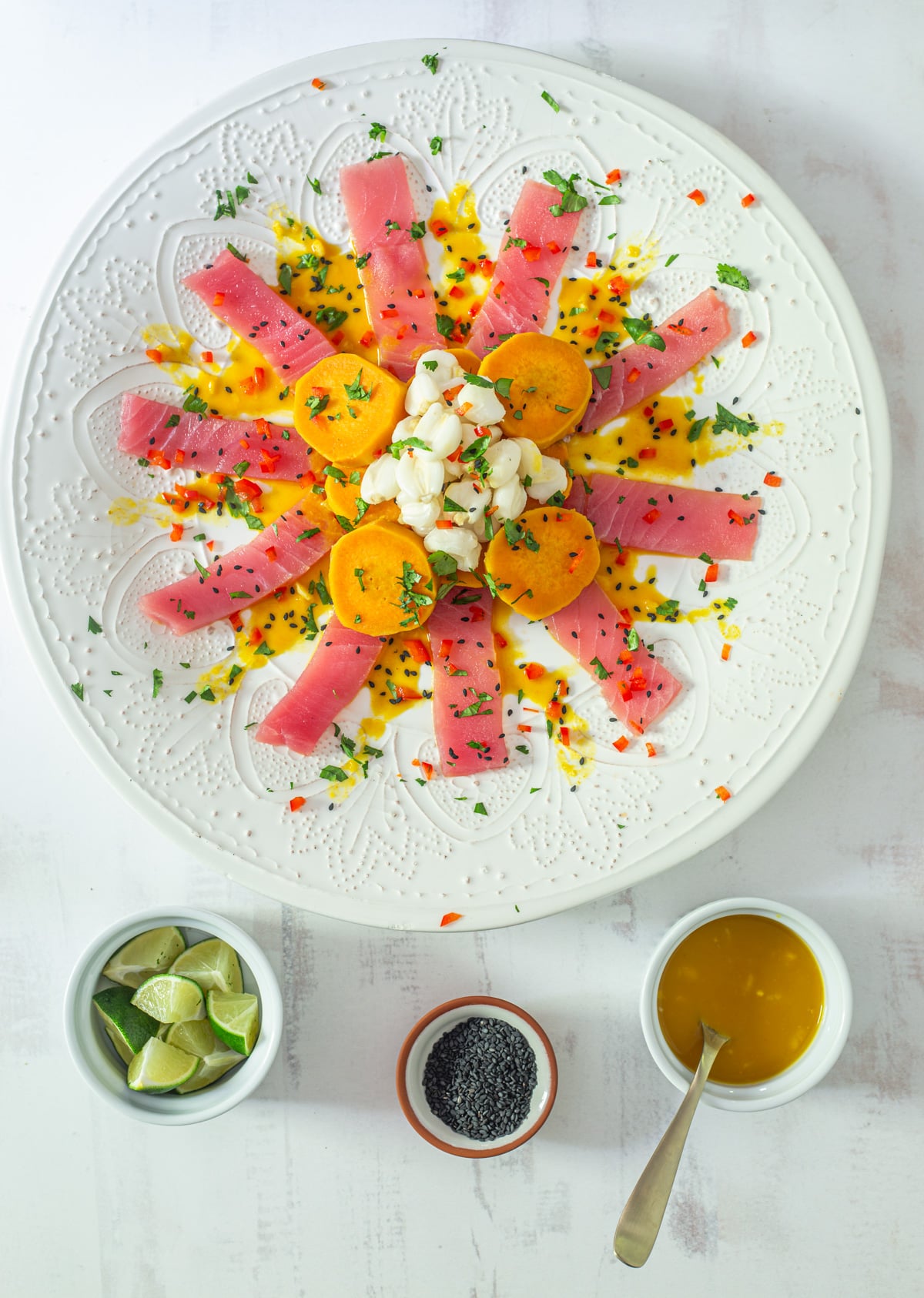 Tiradito de At&uacute;n with garnishes - lime wedges, black sesame seeds, and aj&iacute; amarillo sauce.