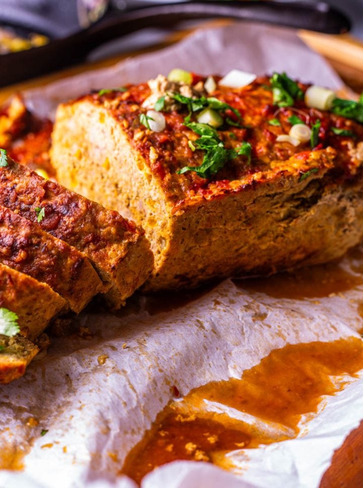 A close up of the healthy Mexican meatloaf on a wood cutting board with juices.
