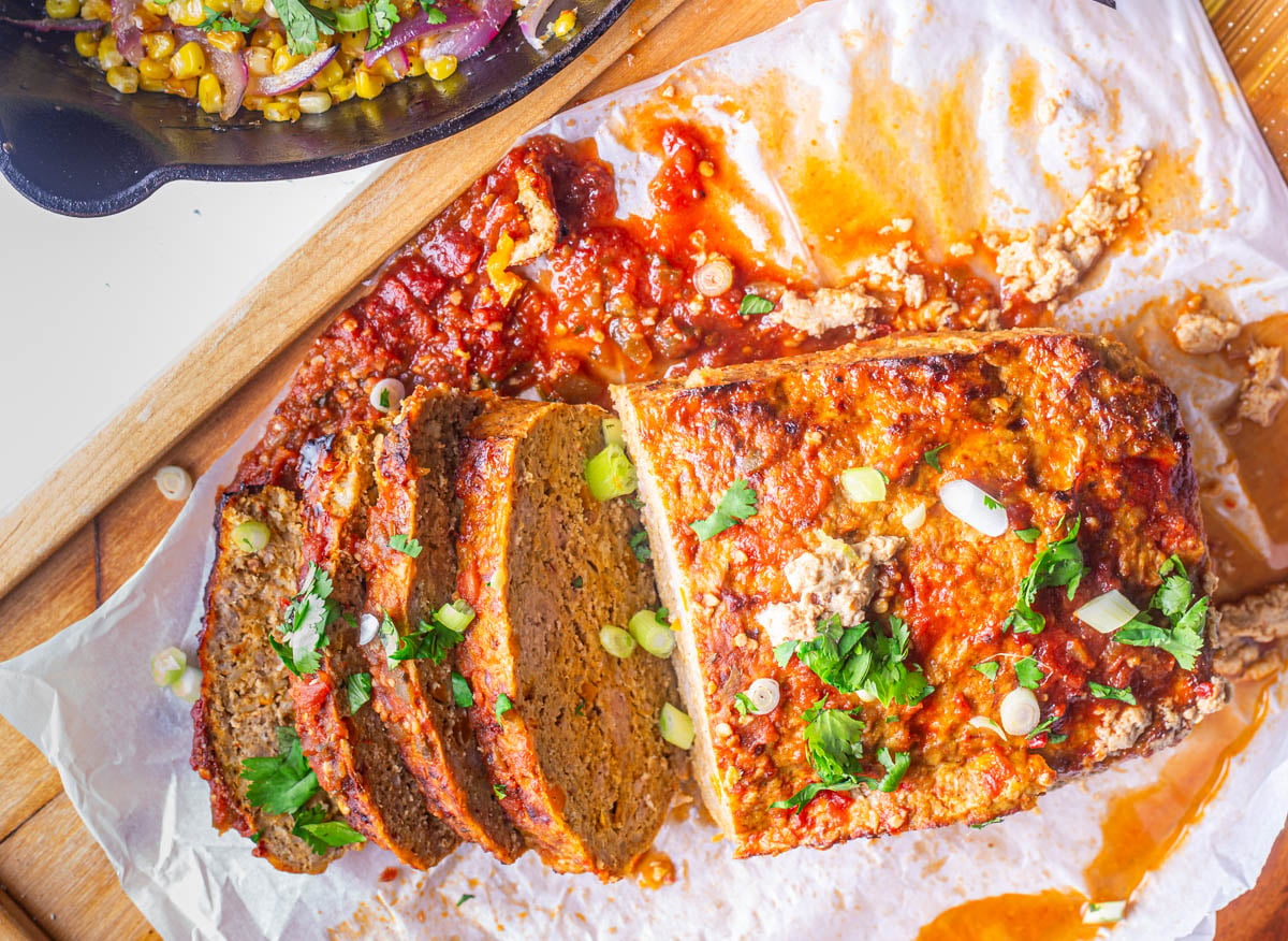 A wood platter with sliced healthy Mexican meatloaf garnished with scallions and cilantro.