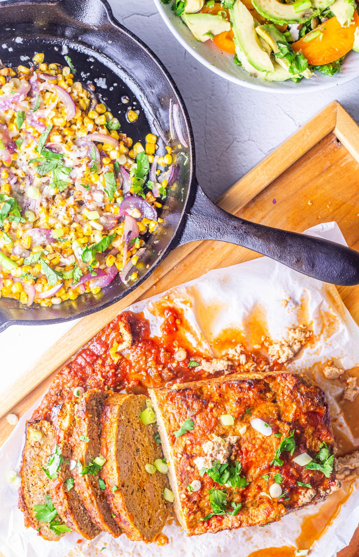 Mexican meatloaf is served with charred sweet corn and a green salad with avocados and tomatoes.