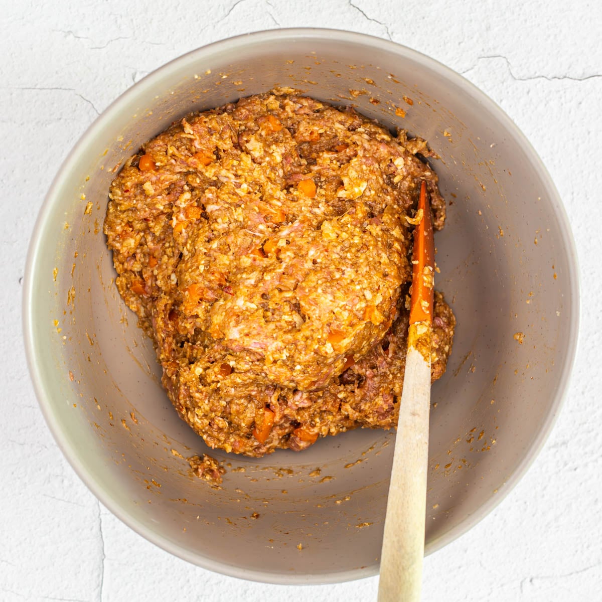 Step 3 - Mexican meatloaf ingredients are thoroughly combine in a large grey prep bowl with an orange spatula.