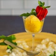 A yellow platter with a single scoop of passionfruit sorbet with mango in a Nick and Nora glass.