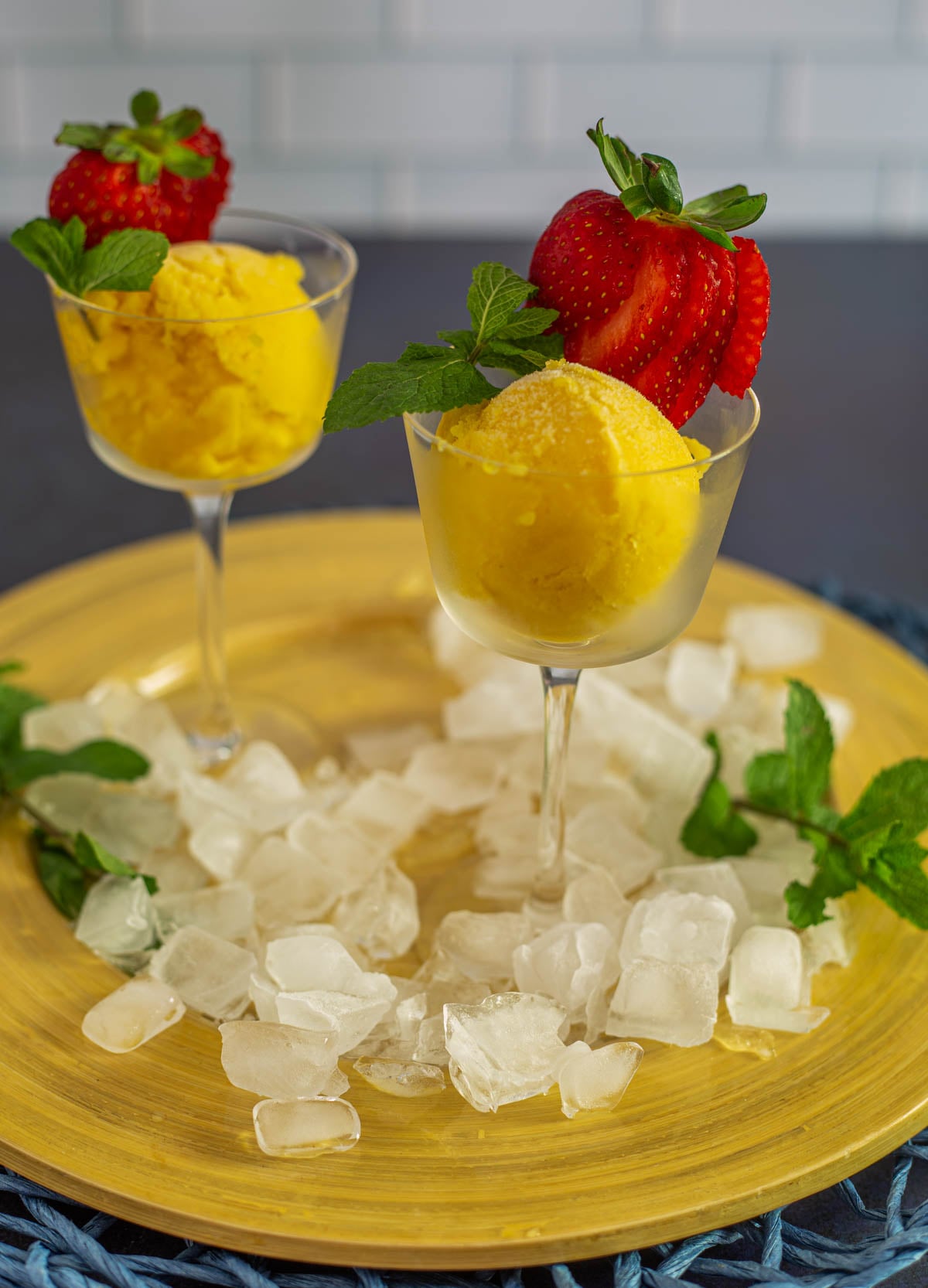 2 Nick and Nora glasses with a scoop of tropical mango passionfruit sorbet garnished with a fresh strawberry and mint.