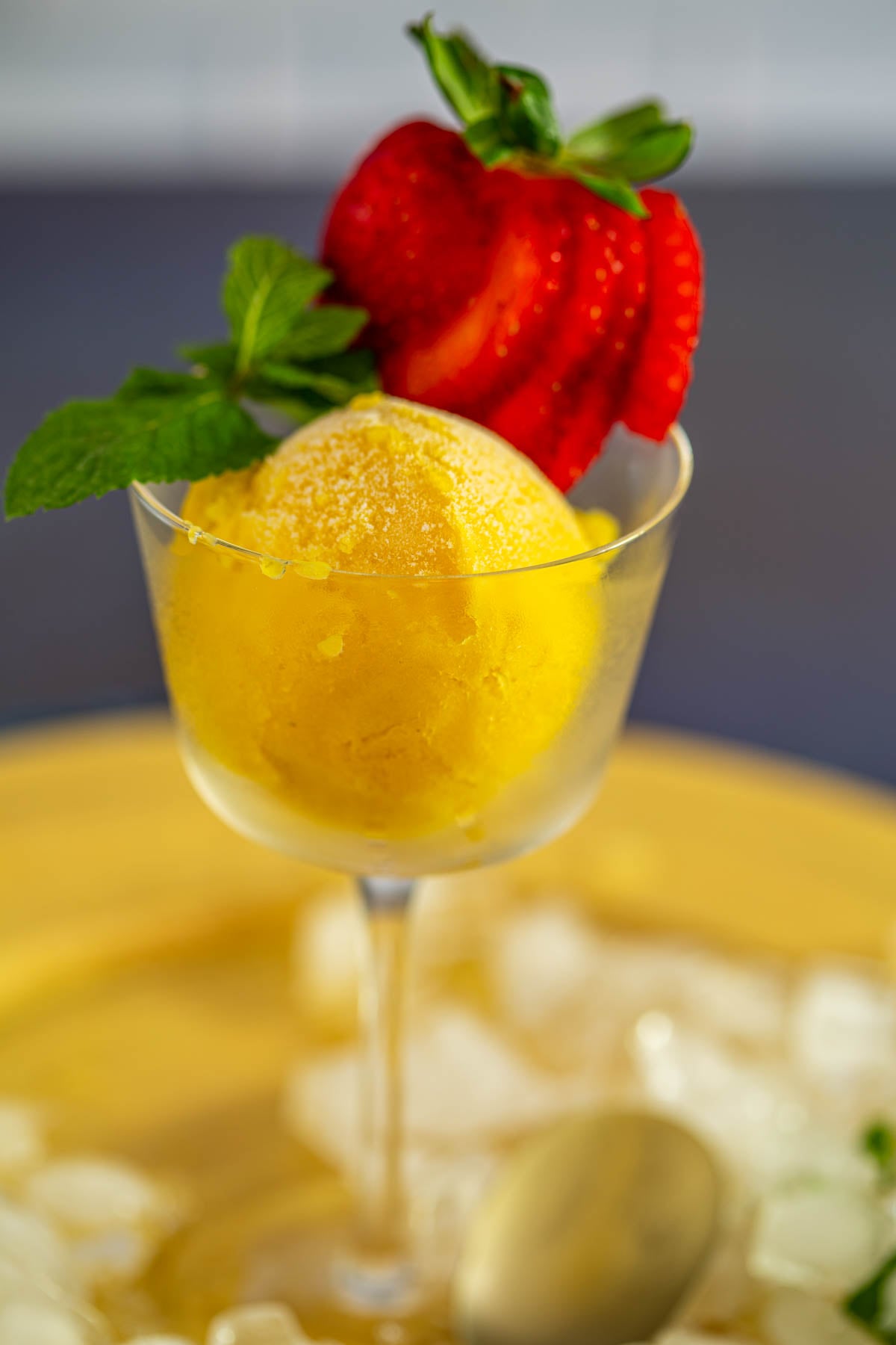 A close up of one creamy scoop of passionfruit sorbet with mangoes and a strawberry fan garnish.