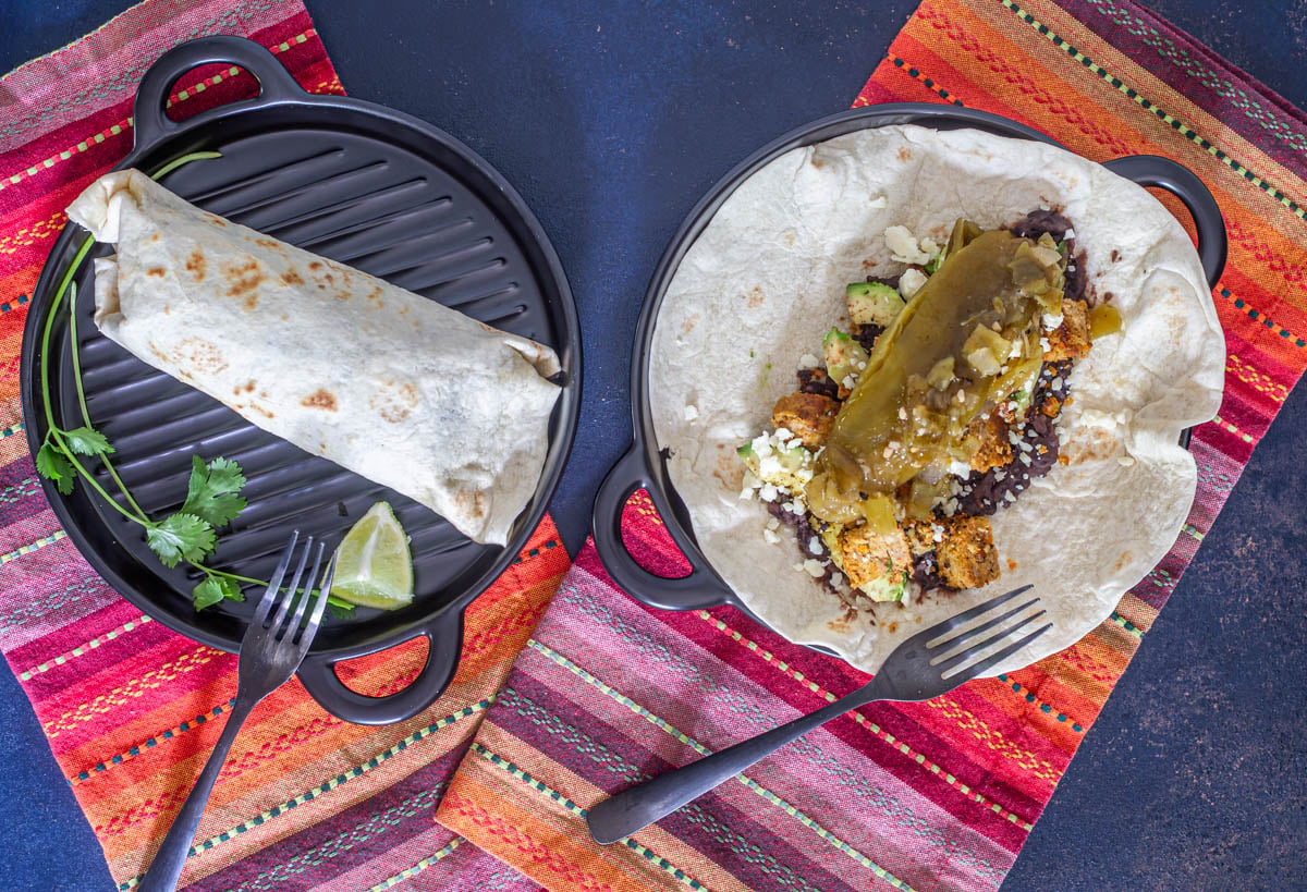2 meatloaf burritos with one completely wrapped, and one open with colorful napkins and forks.