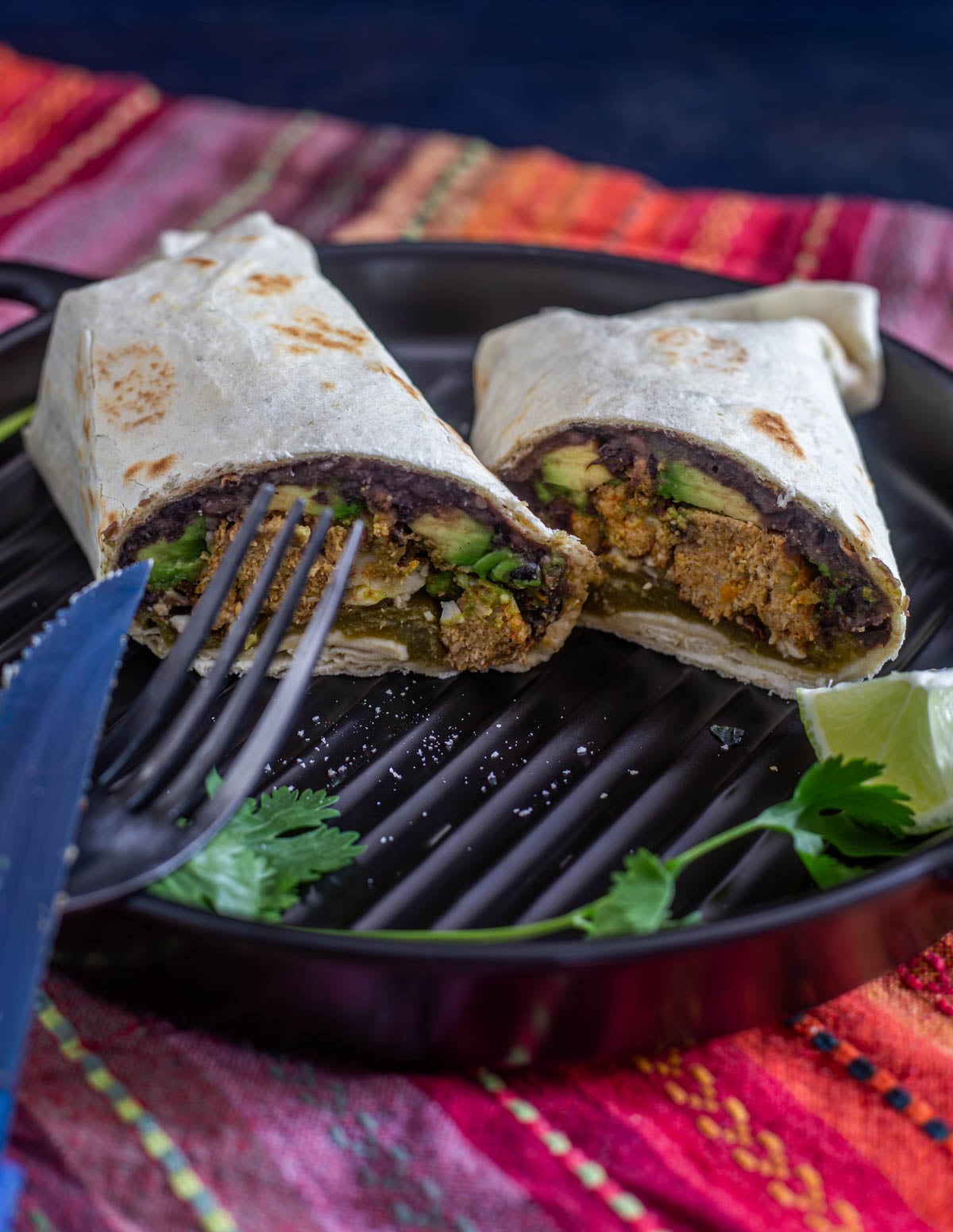 A healthy meatloaf burrito on a black ceramic plate on top of a colorful napkin.