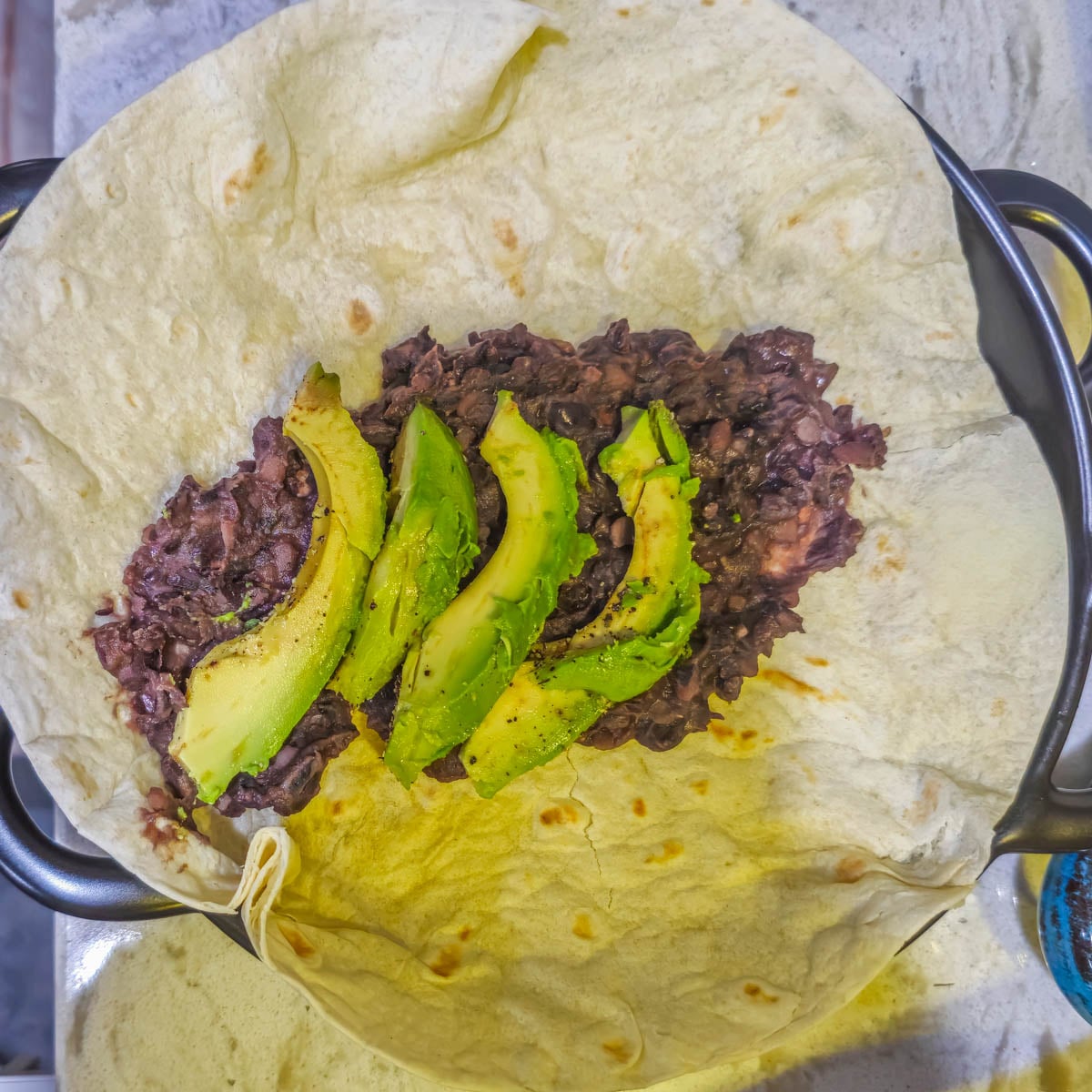 Step 2 - Spread refried black beans in the center of the tortilla and top with sliced avocado.