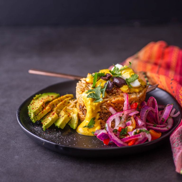 A single arroz tapado portion on a black plate with copper fork and colorful napkin.