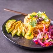 A black stoneware plate with arroz tapado alongside salsa criolla and sliced avocado.