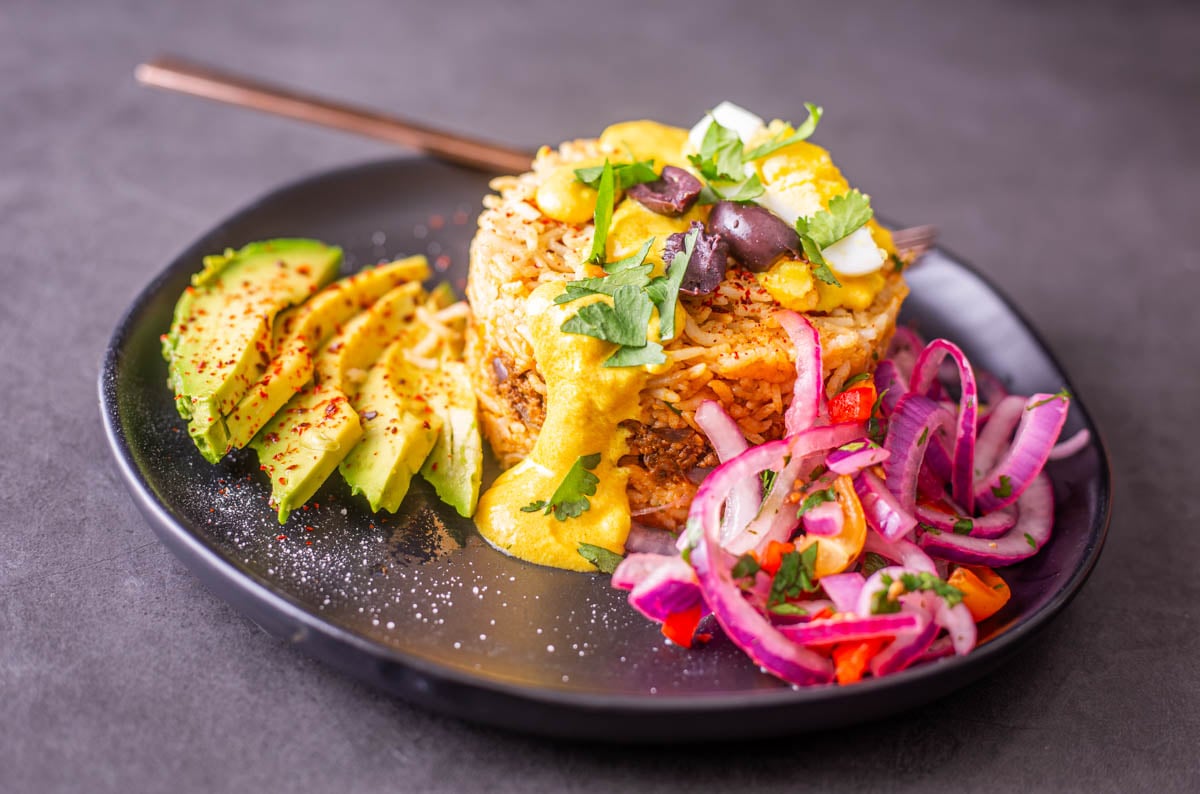 A black stoneware plate with arroz tapado alongside salsa criolla and sliced avocado.