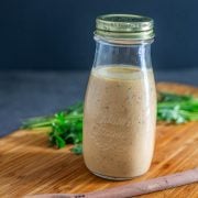 The completed bottle of chipotle ranch dressing in a glass bottle with herbs, wood spoon, and wood cutting board.