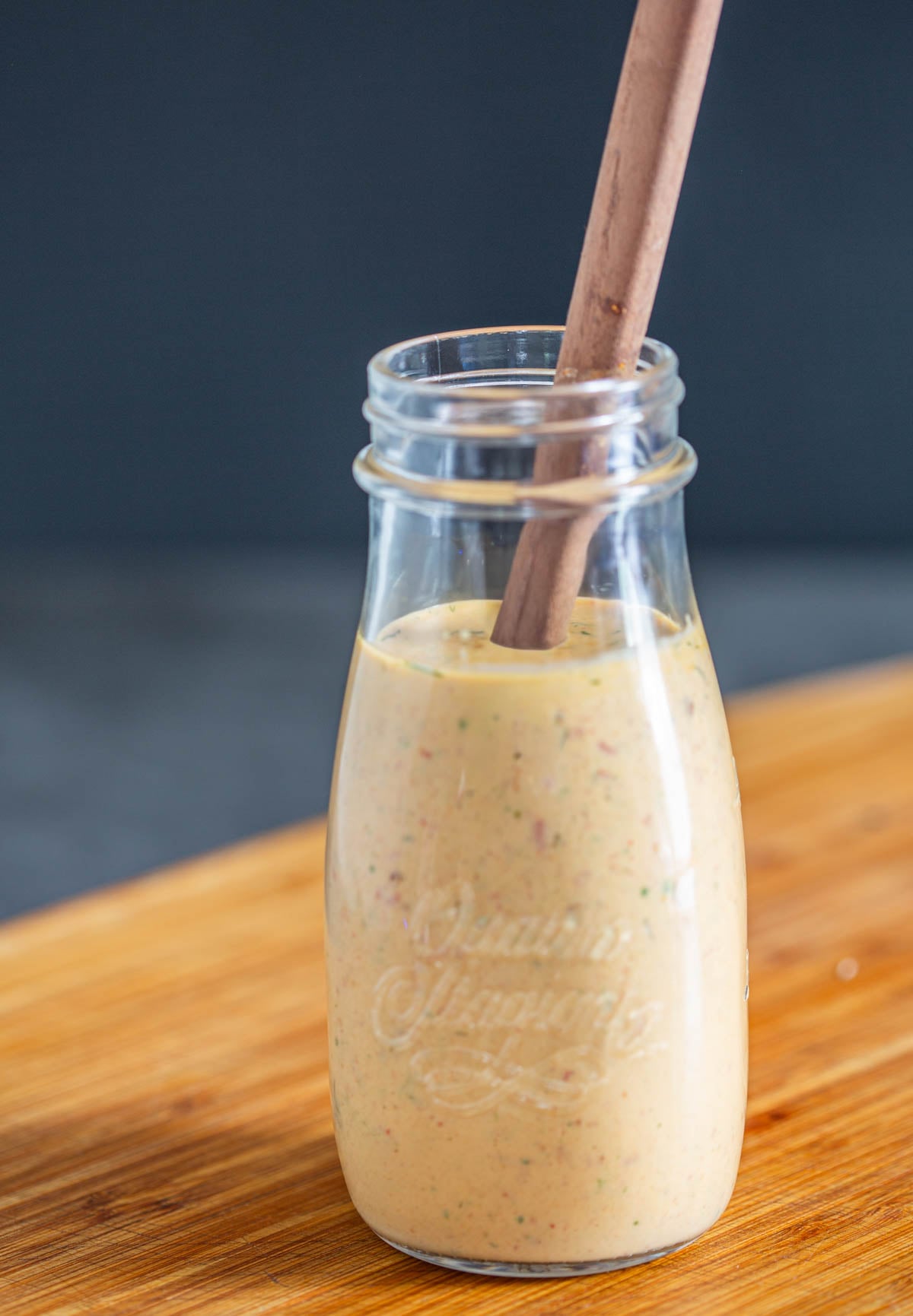 A close up of a glass bottle with chipotle ranch dressing with a wood spoon on a wood cutting board.