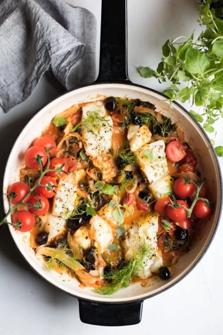 An easy one pan Mediterranean cod with tiny tomatoes in a cast iron pan.