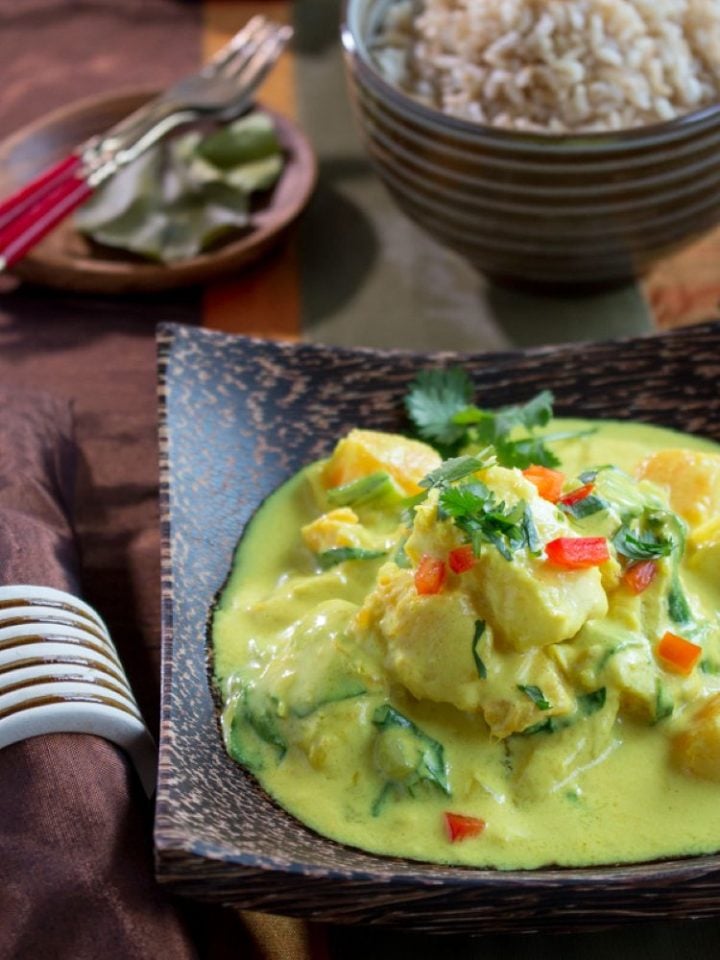 Halibut coconut curry in a square stoneware bowl with a bowl of rice.