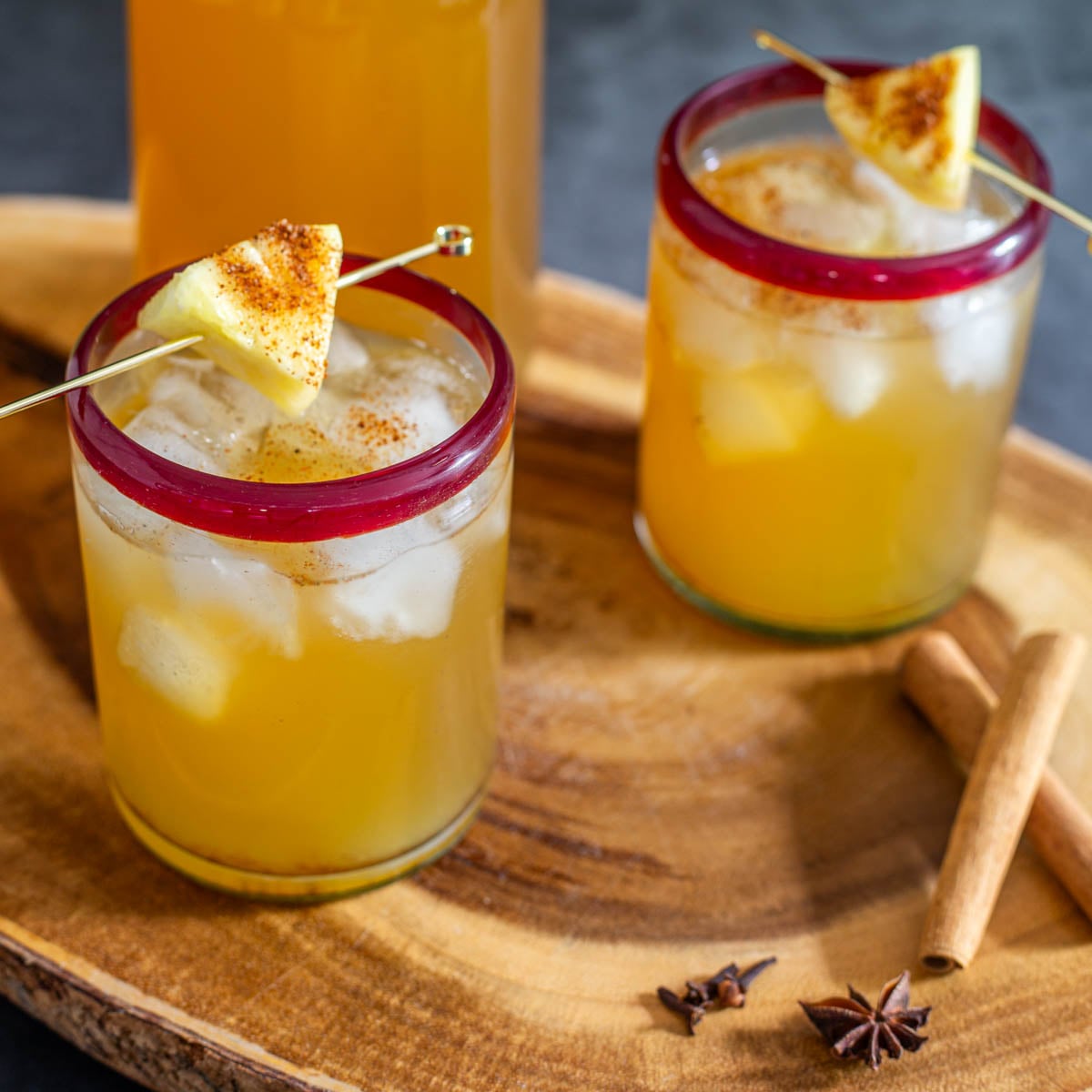 Two red-rimmed glasses of homemade tepache on a wood tray.