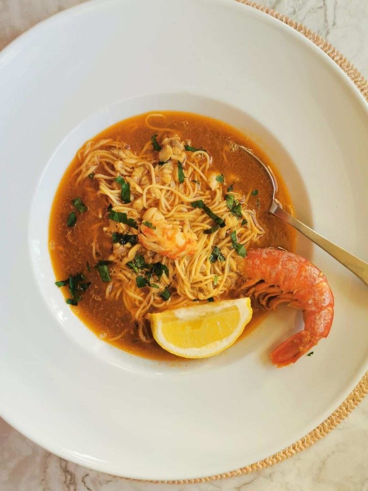 Italian fish soup with angel hair pasta in a white bowl with a giant prawn.