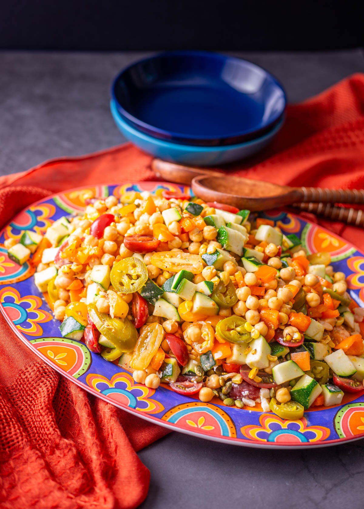 A colorful platter with Mexican chickpea salad shallow ceramic bowls, and wood salad tongs.