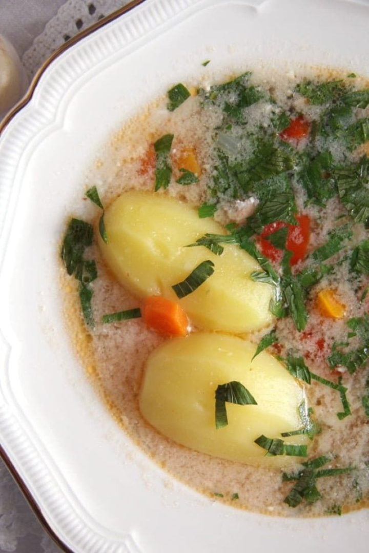 Romanian fish with whole-cooked potatoes, vegetables, and Romanian garlic sauce in a white bowl.