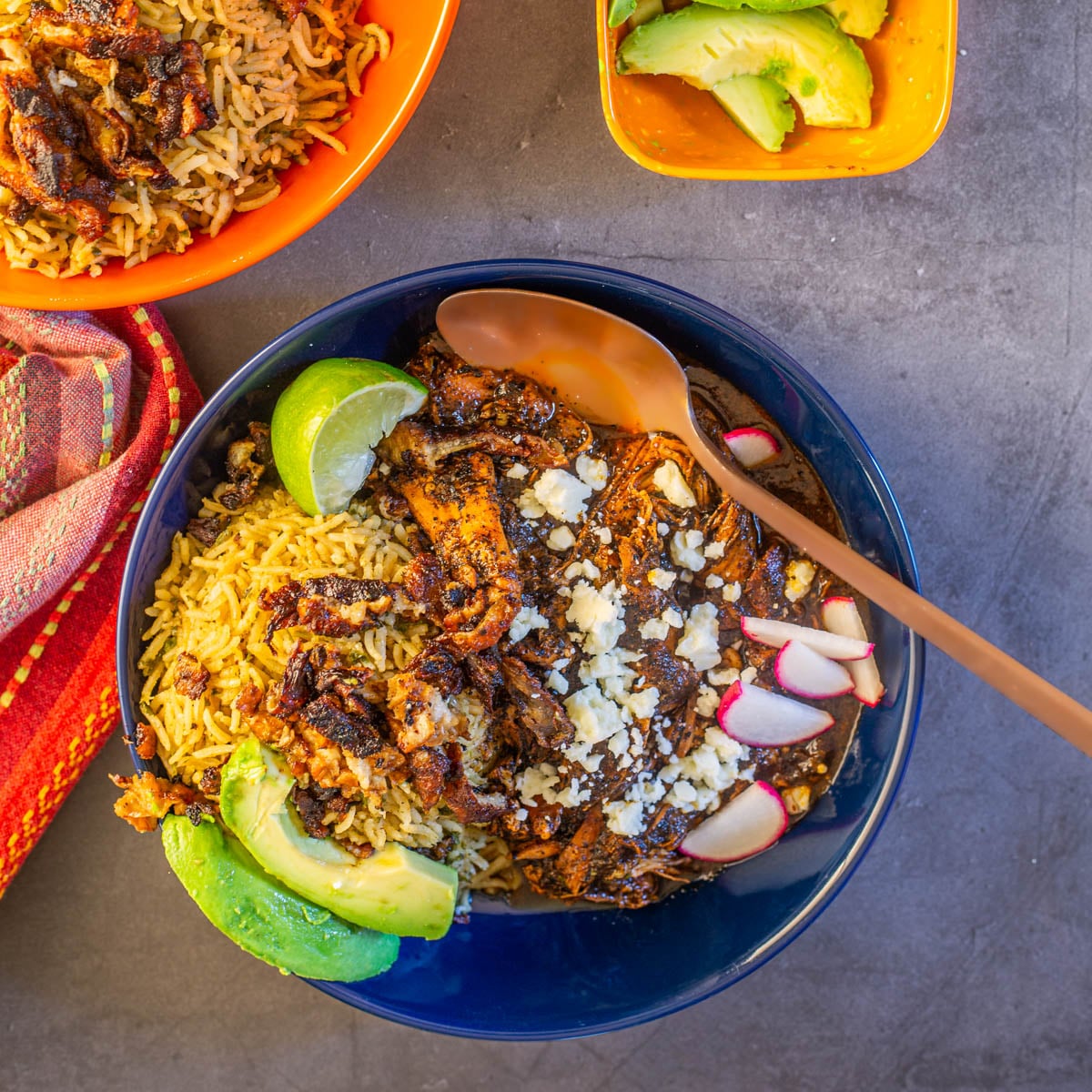 A navy ceramic bowl of chicken birria with cilantro rice and chicharron.