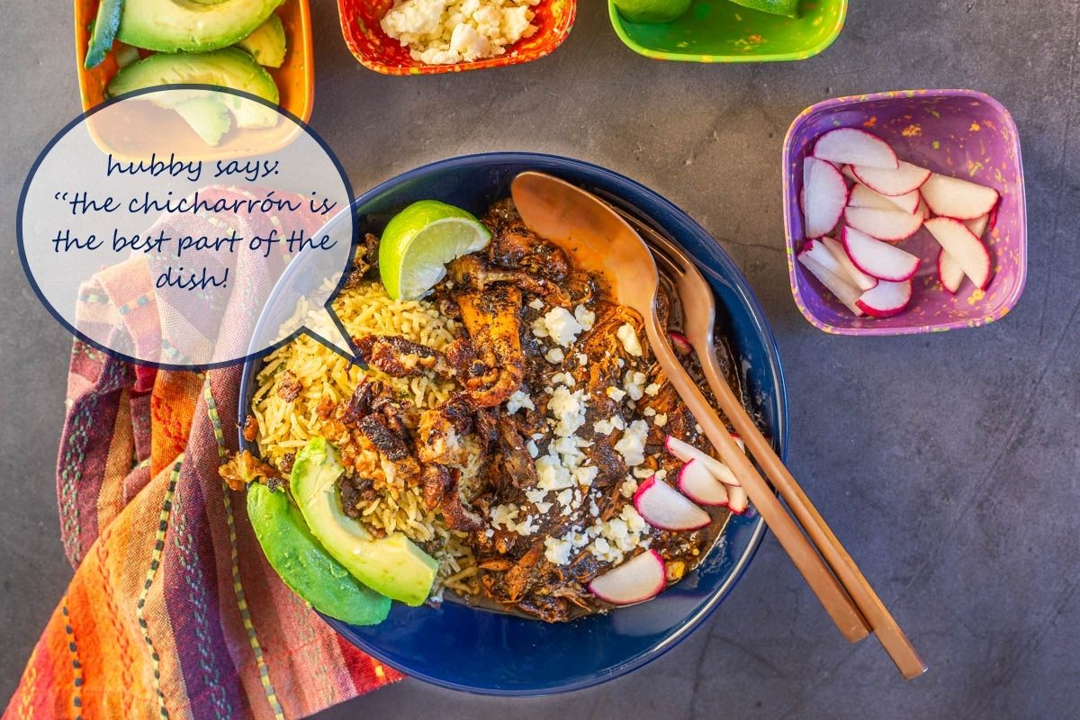 A close up of a navy ceramic bowl of chicken birria with cilantro rice and garnishes.