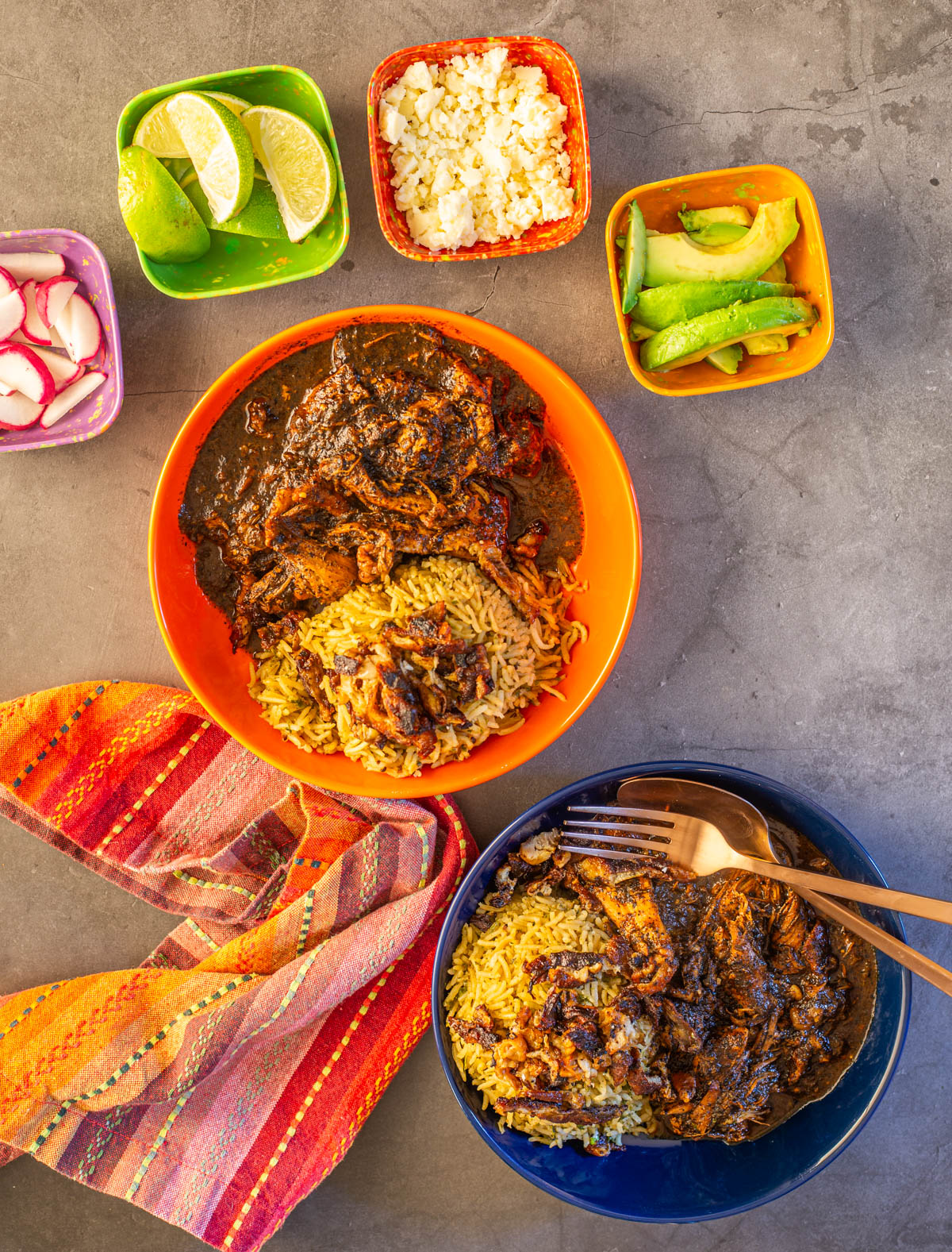 2 colorful shallow bowls with birria de pollo/chicken birria with cilantro rice, chicharron, and garnishes.