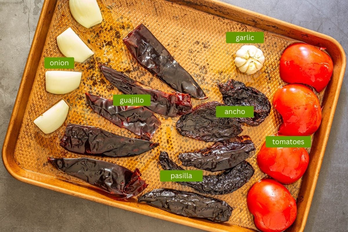 Ingredients for the birrian red chile sauce - Dried red chiles, onion, garlic, and tomatoes on a copper sheet pan.