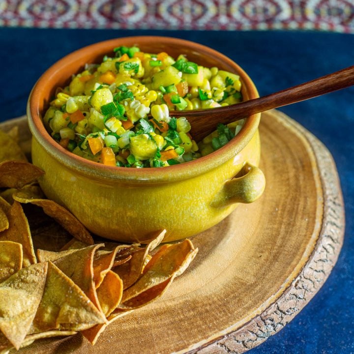 Grilled corn and pineapple salsa in a stoneware bowl with wood spoon.