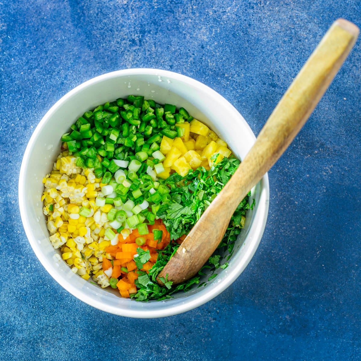 Ingredients for the grilled corn and pineapple salsa in a bowl with a wood spoon.
