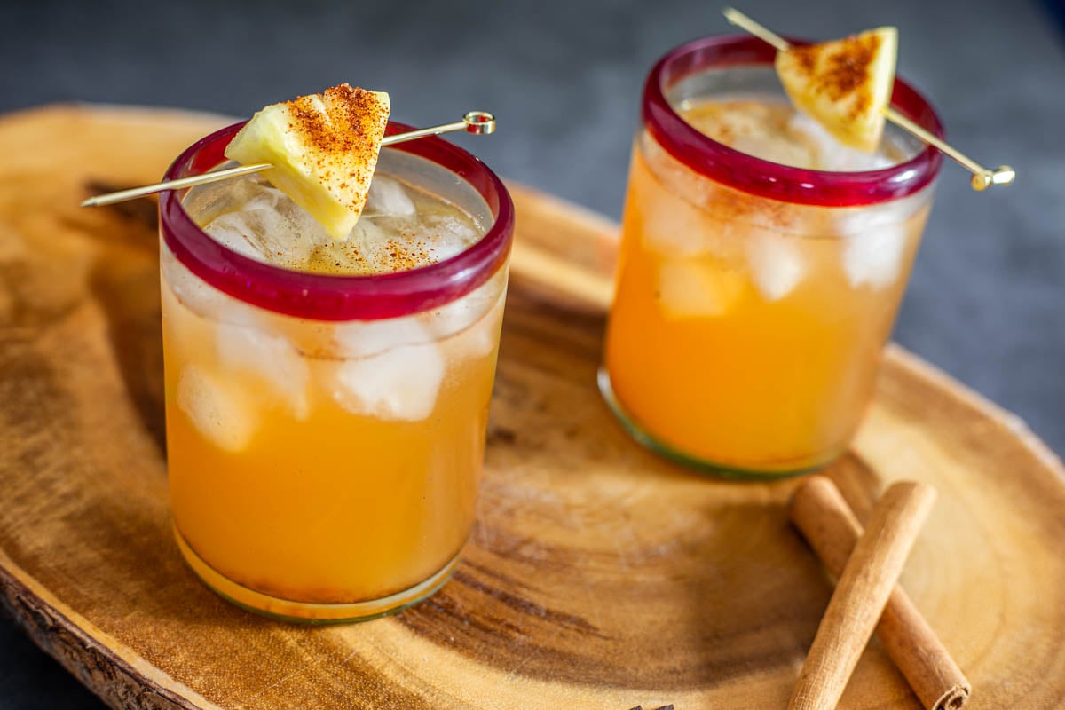 A close up of 2 glasses of homemade tepache on a wood tray.