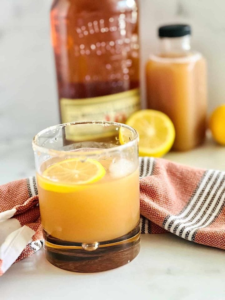An apple cider bourbon cocktail in a rocks glass with ingredients in the background.