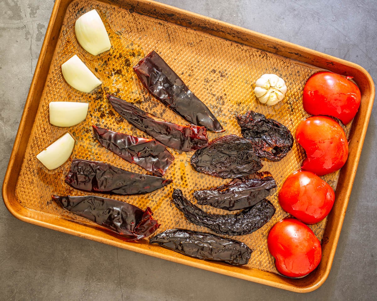 Step 2 - Place tomatoes, onion, and garlic on a sheet pan, then drizzle with oil.