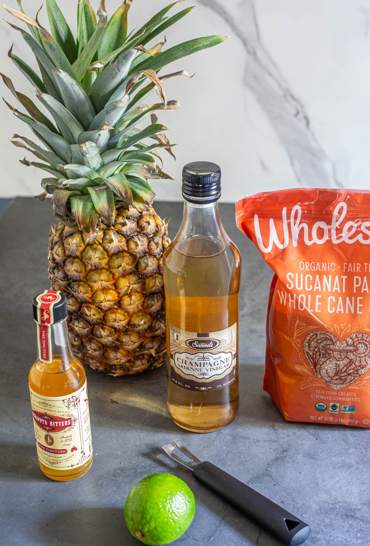Ingredients for the pineaple shrub including a fresh pineapple, champagne vinegar, granulated panela, lime, and Scrappy's fire tincture bitters.