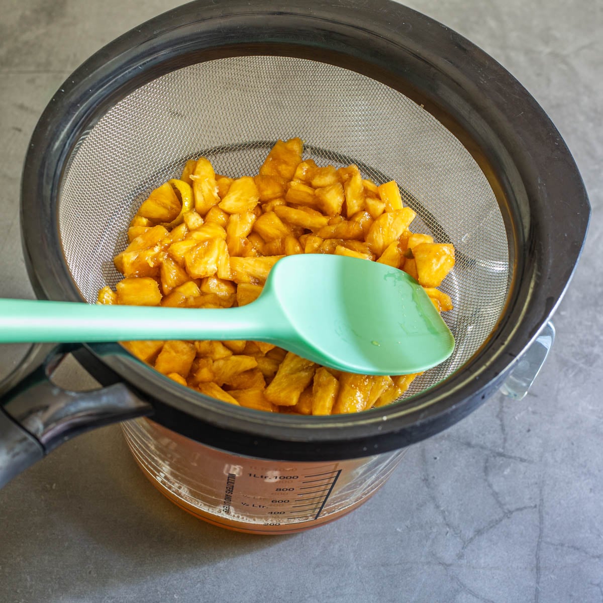 The mascerated pineapple and lime peel are pressed through a fine mesh sieve into a glass bowl.
