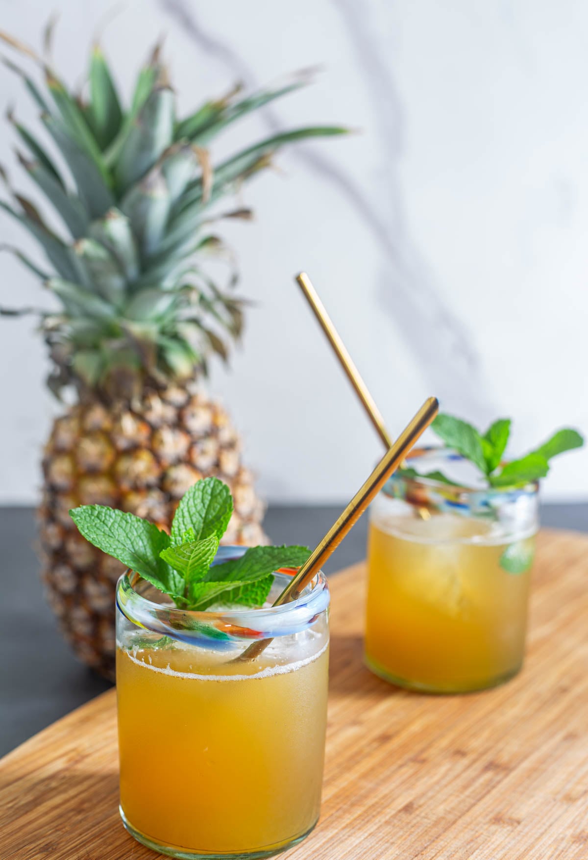 Two glasses of pineapple shrub and soda garnished with mint and a pineapple.